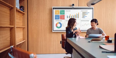 Two women in business attire looking at charts on a display.