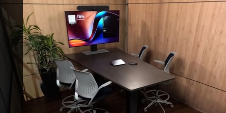 A modern conference room with a large display, mounted camera, conference table, and seating for multiple participants.