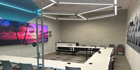 conference room with tables aligned in a u-shape in front of a large double display with conferencing cameras around.
