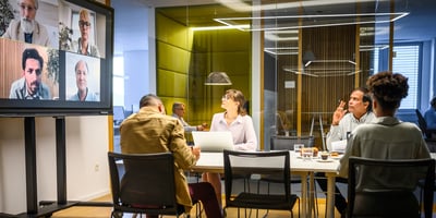 Group of people sitting down at a table with Team meeting in progress with a colorful background.