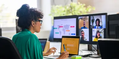 A professional participating in a virtual meeting from a home office, collaborating with remote colleagues across multiple screens displaying a video conference, digital workspace, and global project content.