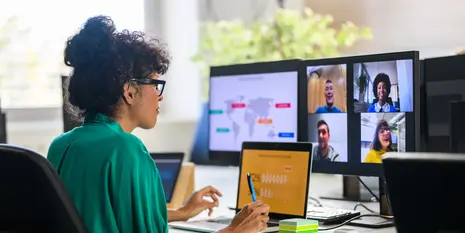 A professional participating in a virtual meeting from a home office, collaborating with remote colleagues across multiple screens displaying a video conference, digital workspace, and global project content.