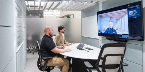 two men in a small conference room looking at a display with a women