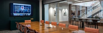 modern corporate conference room in the foreground with a glass wall separating a common area in the background
