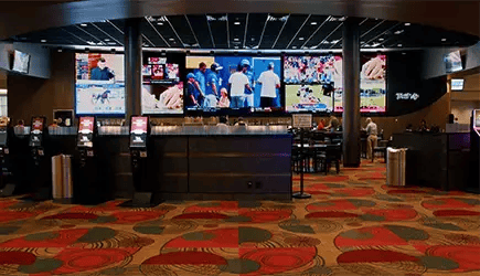 Entrance to a casino bar and dining area with a large LED display showing sports in the background.