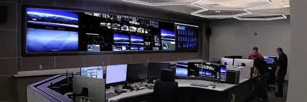 Multi-functional LED display wall above workstations with multiple monitors.