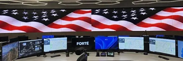 Large, curved LED display wall featuring an American flag above seven computer monitors.
