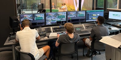 Three students sitting behind a broadcast booth controlling the AV systems at Westminster Schools
