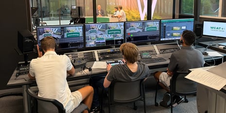 Three students sitting behind a broadcast booth controlling the AV systems at Westminster Schools