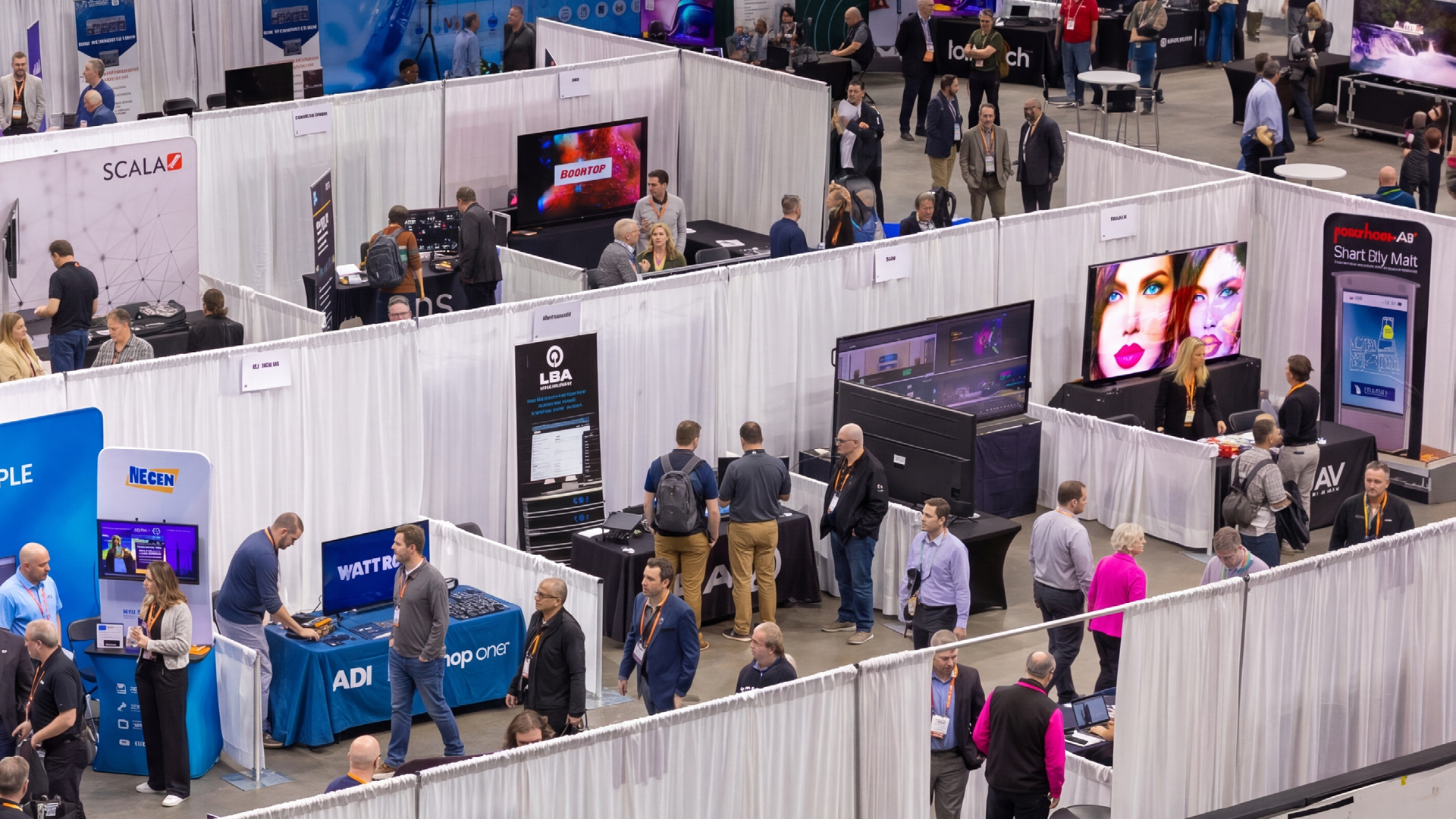 Wide view of a busy AV and technology trade show floor with exhibitor booths, large digital displays, and attendees networking and exploring products throughout the expo hall.