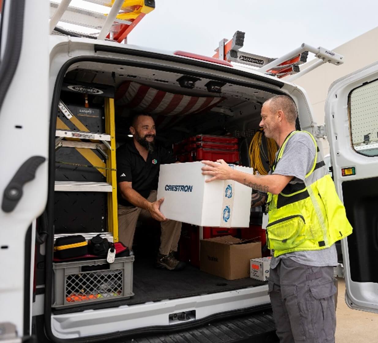 Two men loading professional AV equipment into a truck, with one guiding and lifting while the other positions the gear for safe transport.