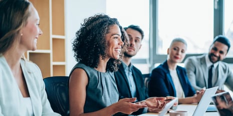 Five people lined up in a boardroom setting while a professionally dressed woman speaks to the group.