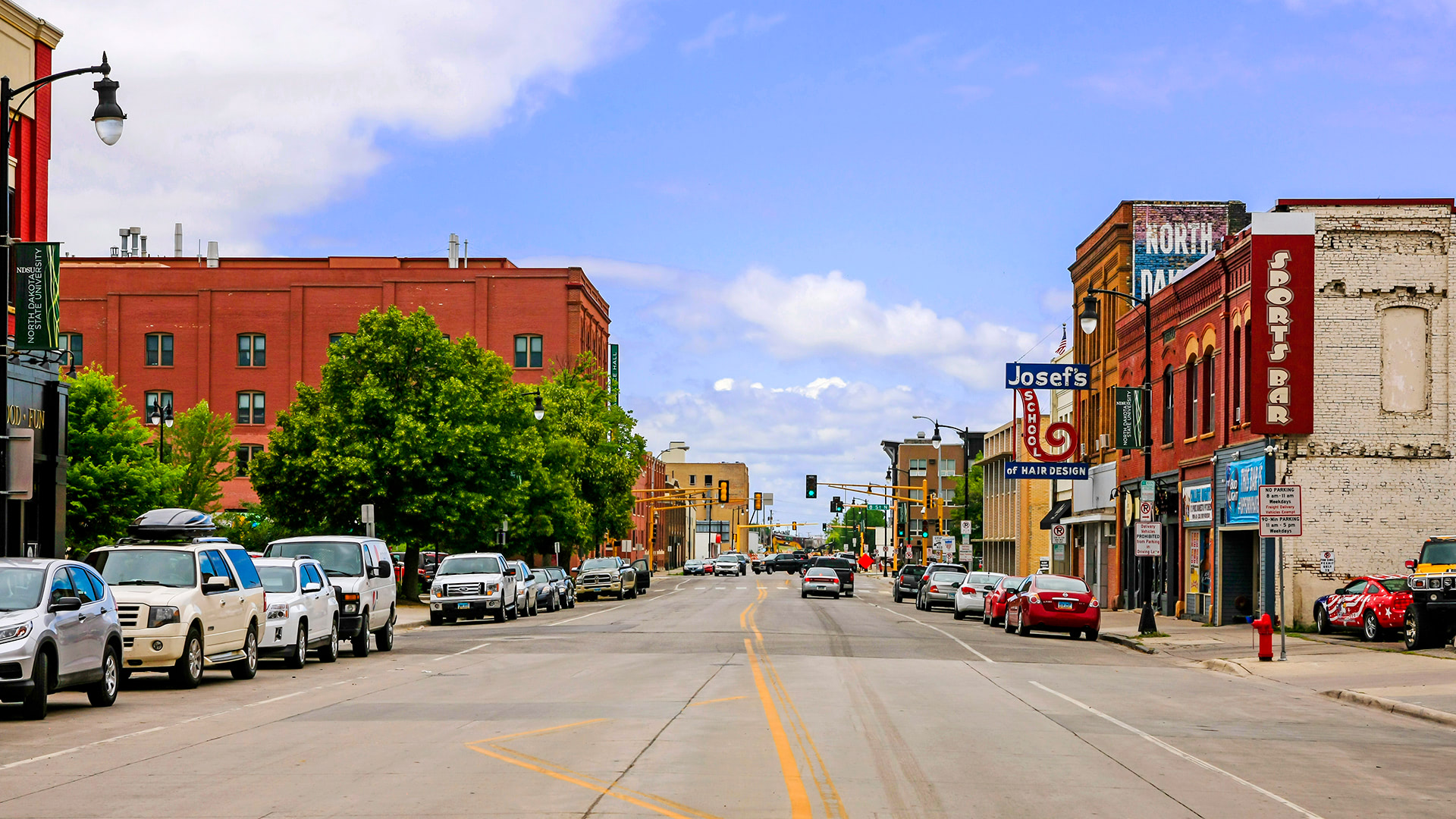 A busy city street with parked cars, shops, and a clear sky, representing urban environments FORTÉ operates in.