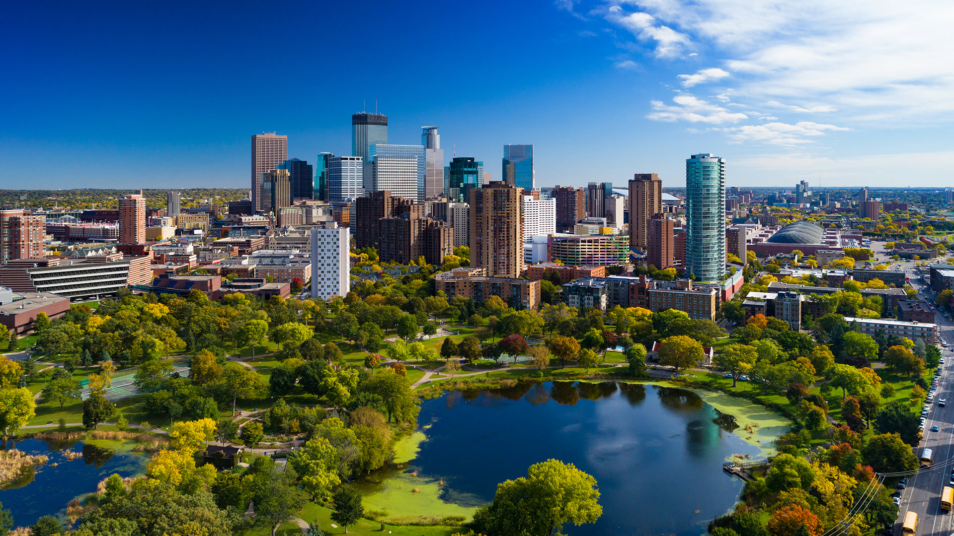 Aerial view of a vibrant city skyline with lush green parks and a serene pond, highlighting modern urban integration.